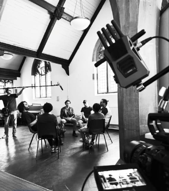 Cast and crew gathered on a film set, with camera equipment in the foreground