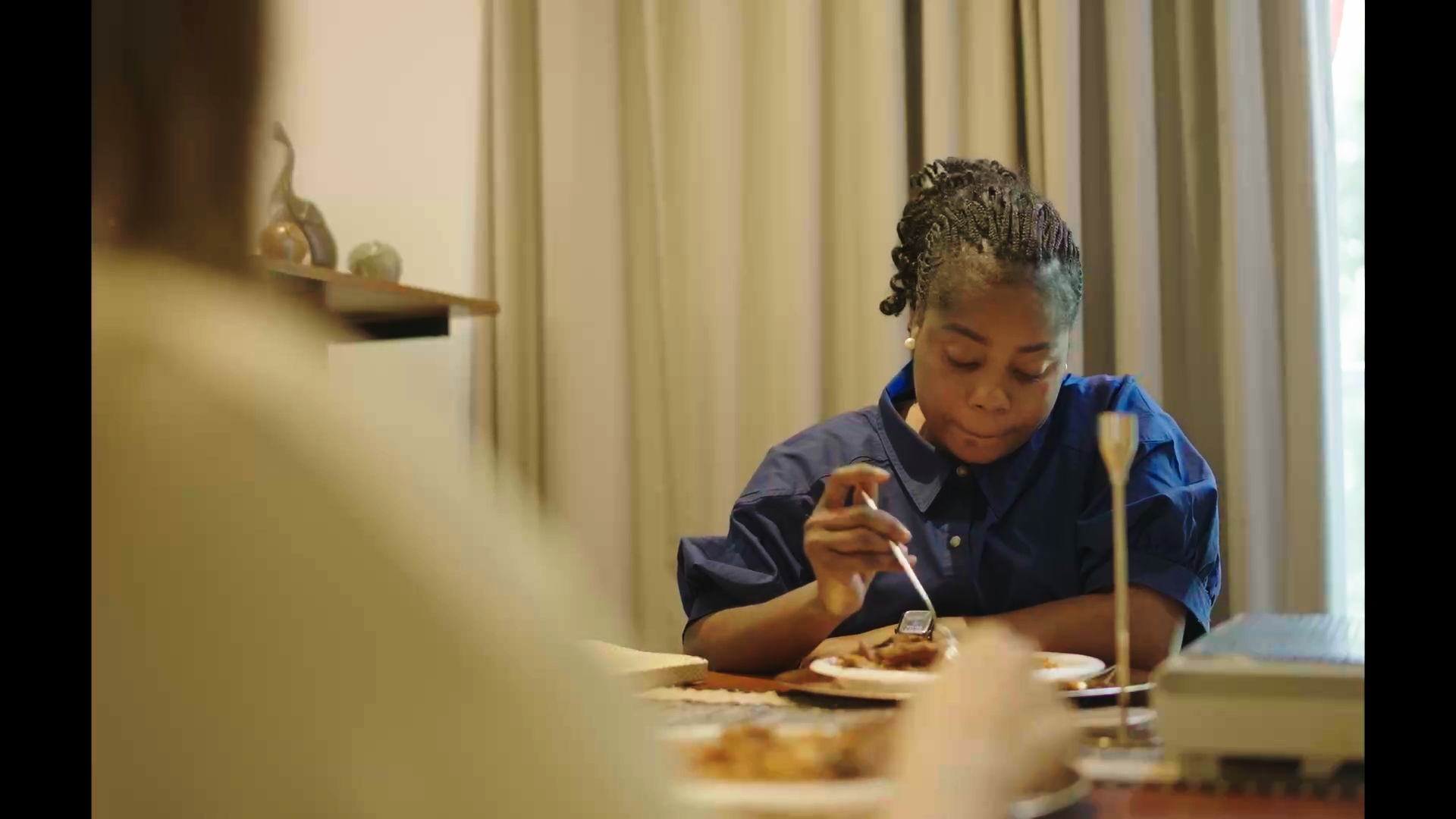 Unbecoming / Serwaa: A woman seated at a dining table