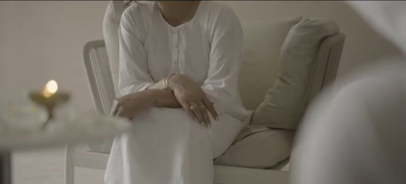 Entrapment: A woman in white seated indoors